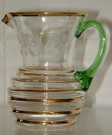 Unknown small milk or cream jug
Unknown maker. Clear glass with gold lines, green applied handle, and white floral pattern around top. This is the same shape as the large Seneca Streamline pattern jug.
